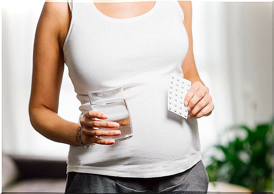 Pregnant woman with a glass in one hand and pills in the other